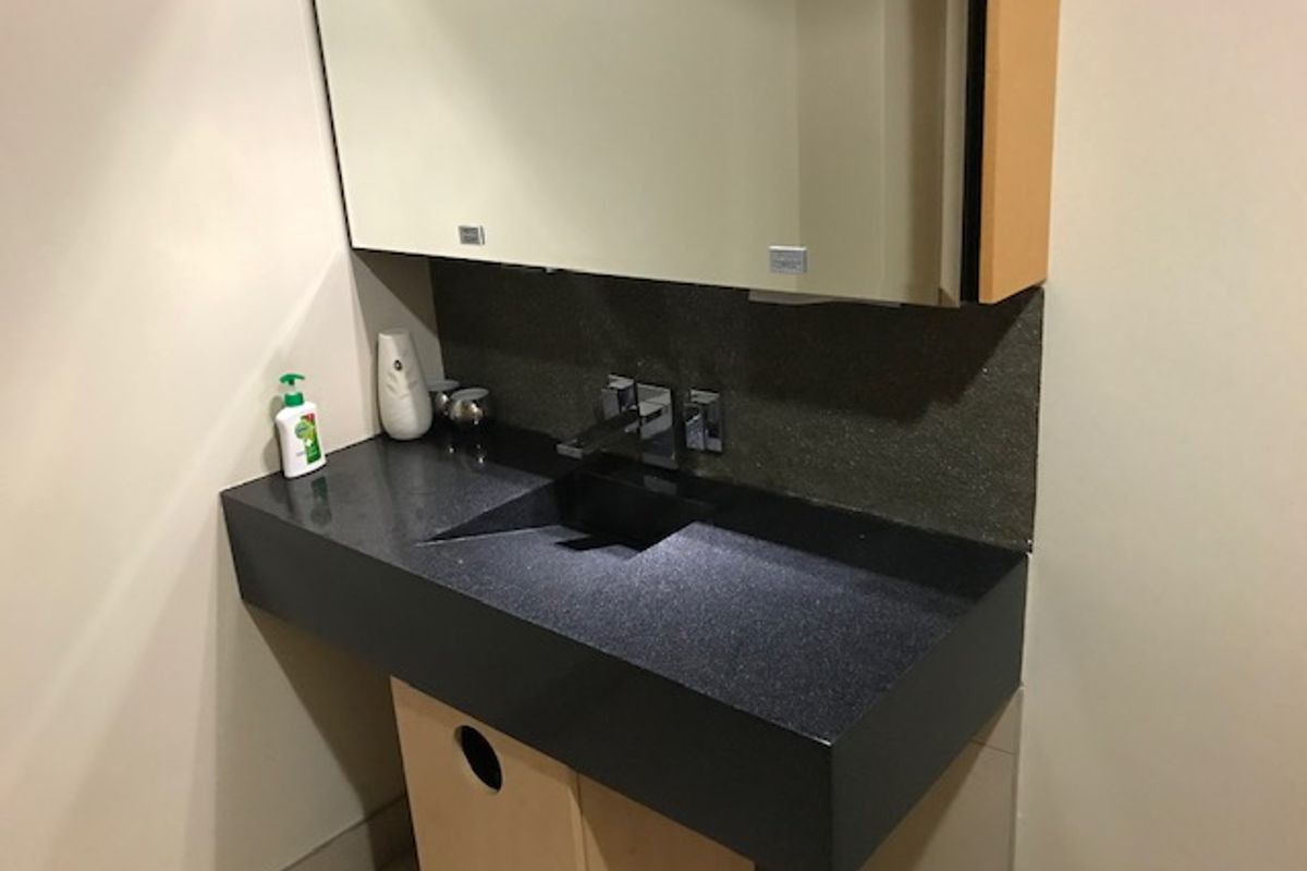A modern office bathroom featuring a sleek black stone vanity countertop with an integrated sink, chrome faucet, and a large wall-mounted mirror cabinet.