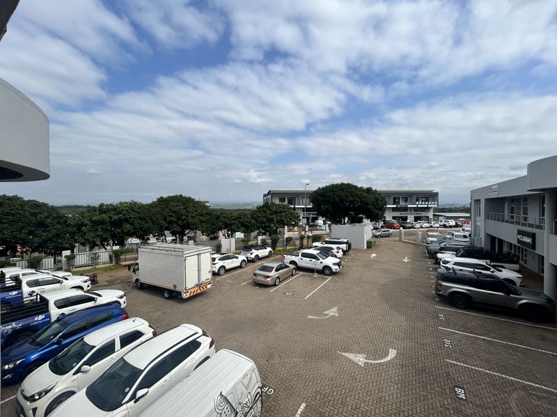 An elevated view of a paved commercial parking lot serving office buildings, featuring marked bays and perimeter fencing.