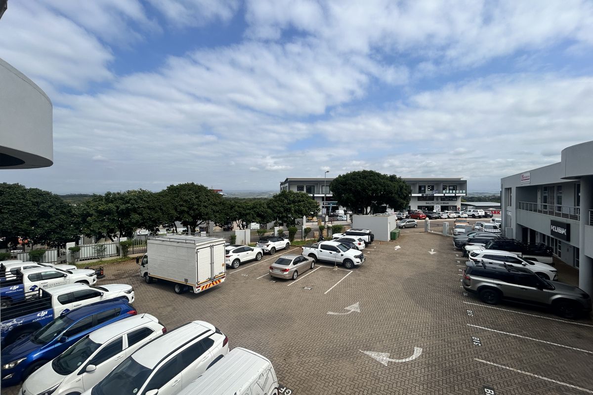 An elevated view of a paved commercial parking lot serving office buildings, featuring marked bays and perimeter fencing.