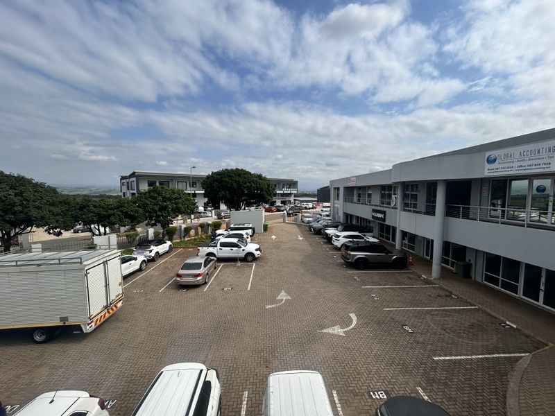 An elevated view of a commercial office complex featuring a paved parking lot and multi-level building facades with balcony access.