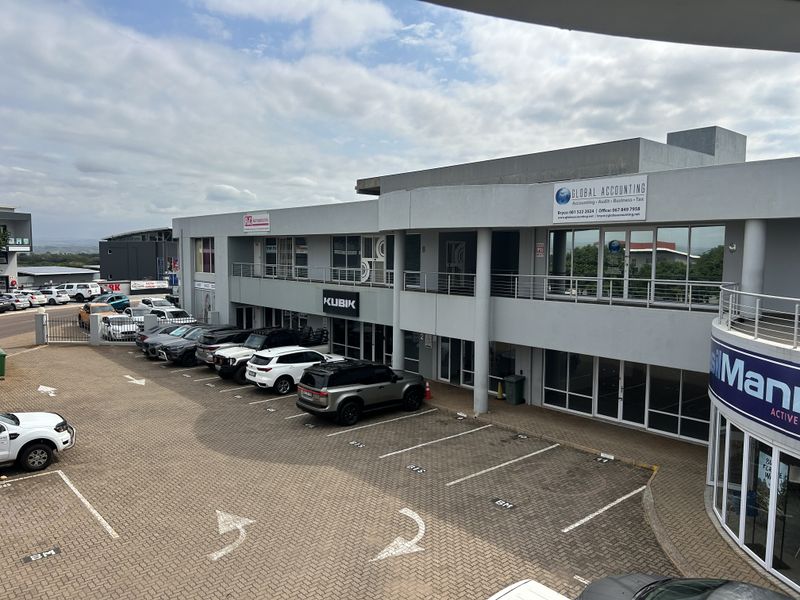An elevated view of a modern multi-level office complex featuring paved parking, glass storefronts, and professional signage.