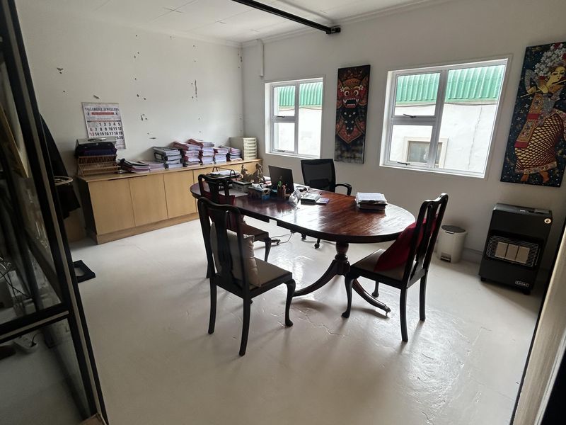 A functional office space featuring built-in cabinetry, uPVC windows, and a suspended ceiling, currently showing signs of wear on the walls and ceiling.