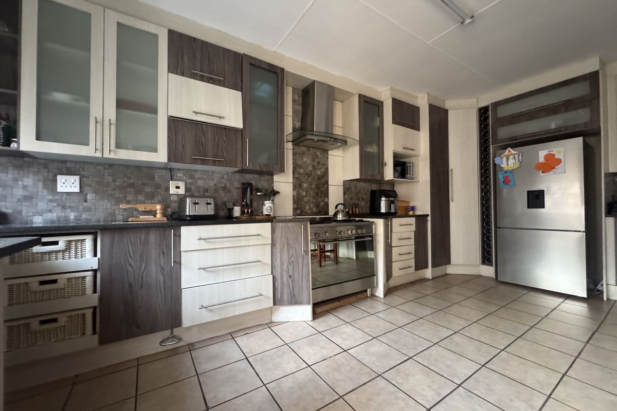 A functional kitchen featuring two-tone cabinetry, mosaic tile backsplash, stainless steel extractor fan, and tiled flooring.