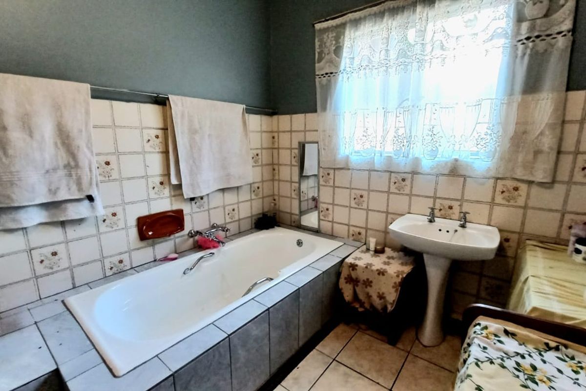 A dated bathroom featuring a built-in bathtub with tiled surround and a classic pedestal basin, requiring modernization of finishes.