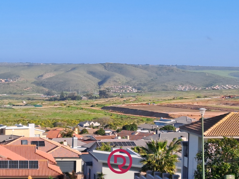 Elevated view overlooking a residential neighborhood with rolling hills in the background, showcasing surrounding landscape and rooftops.