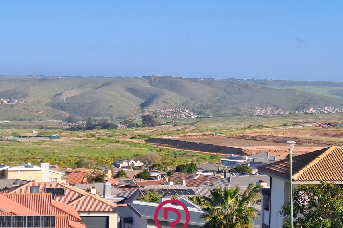 Elevated view overlooking a residential neighborhood with rolling hills in the background, showcasing surrounding landscape and rooftops.