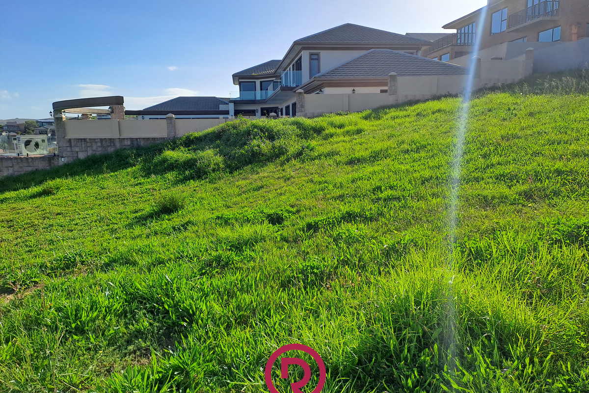 A sloped residential vacant land plot featuring established boundary walls and views of neighboring properties.