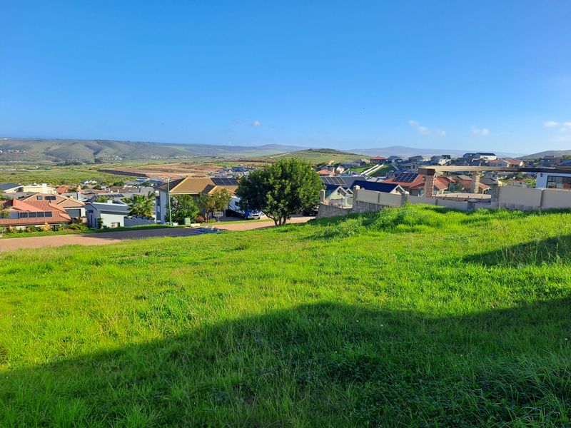 A scenic view overlooking a residential neighborhood and surrounding landscape from a vacant, grass-covered residential plot.