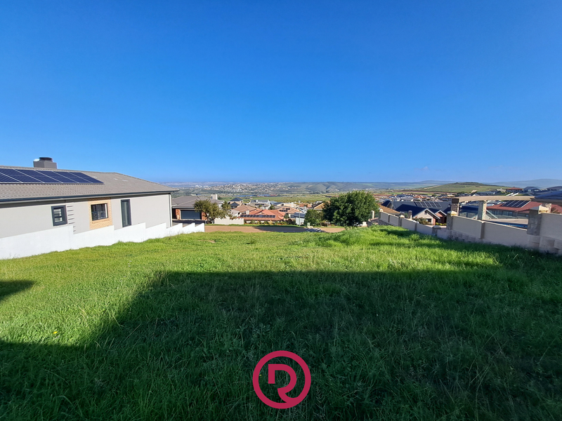 A vacant residential plot featuring a gentle slope, boundary walls, and expansive views of the surrounding neighborhood and landscape.