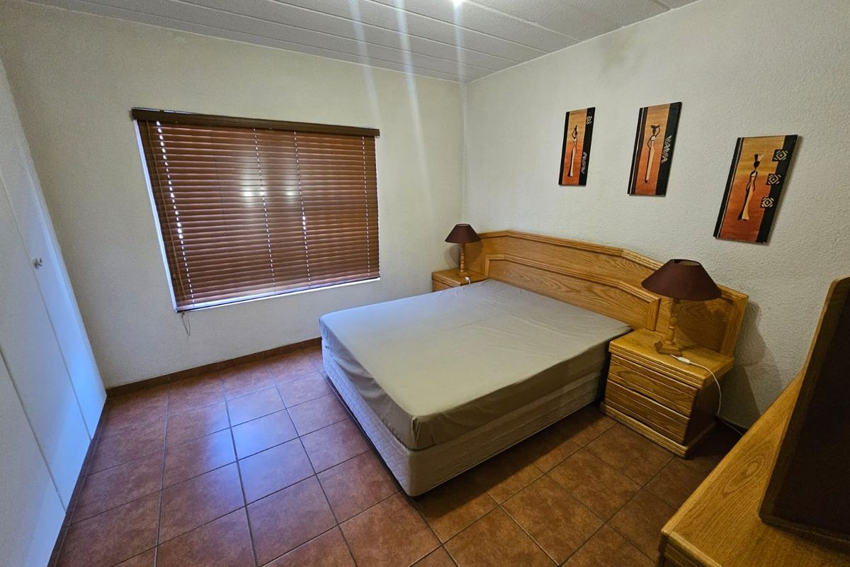 A bedroom featuring tiled flooring, built-in cupboards, and a window fitted with wooden blinds.