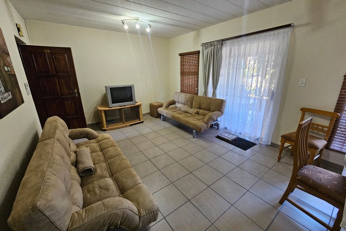 A living room featuring tiled flooring, a sliding glass door with security gate, and a wooden door leading to other areas of the townhouse.
