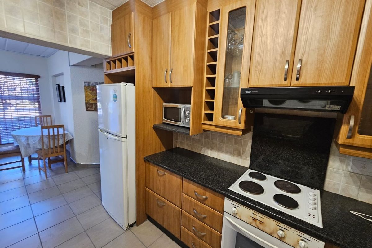 A functional kitchen featuring wood-veneer cabinetry, dark granite countertops, a built-in electric hob, and an extractor fan, with tiled flooring throughout.