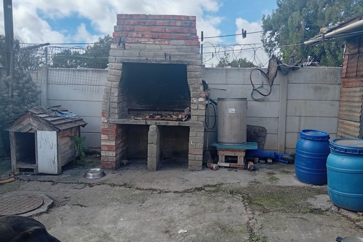 Rear outdoor area featuring a built-in brick braai and concrete paving, enclosed by a precast concrete boundary wall.