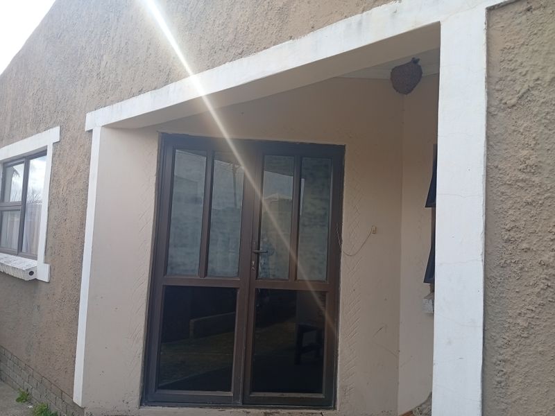 Front entrance area featuring an aluminium framed glass door and window with a covered porch, showing signs of wear and exterior maintenance requirements.