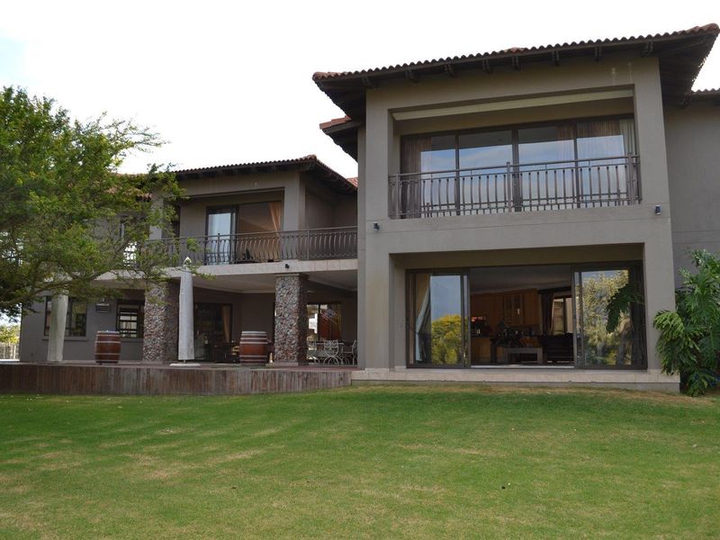 A spacious two-story rear elevation featuring a large covered patio, expansive lawn, and upper-level balconies with sliding glass doors.