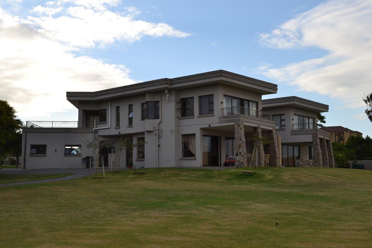 A spacious multi-story residential property featuring stone-clad pillars, expansive balconies, and large windows, set within a well-maintained garden area.