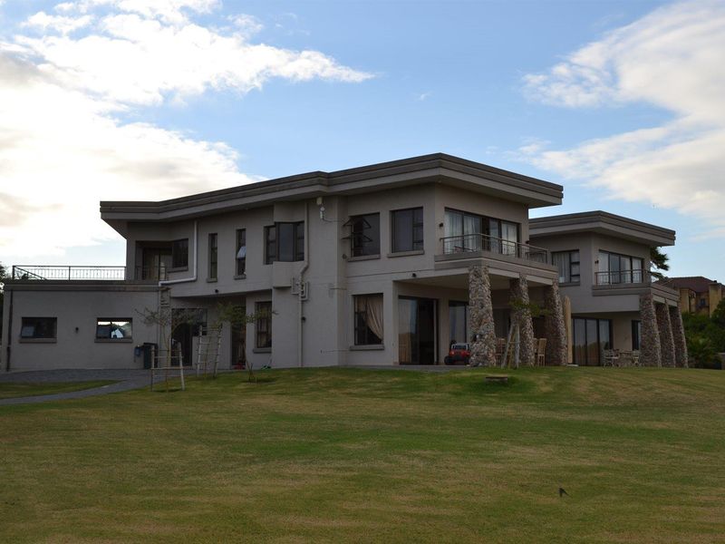 A spacious multi-story residential property featuring stone-clad pillars, expansive balconies, and large windows, set within a well-maintained garden area.