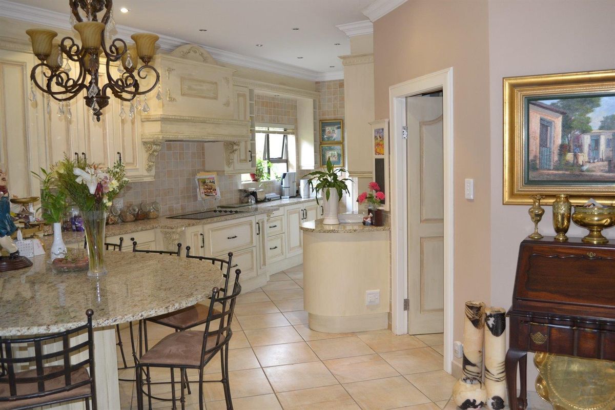 A traditional kitchen featuring ornate cabinetry, granite countertops, a built-in hob, and a central island with integrated seating.