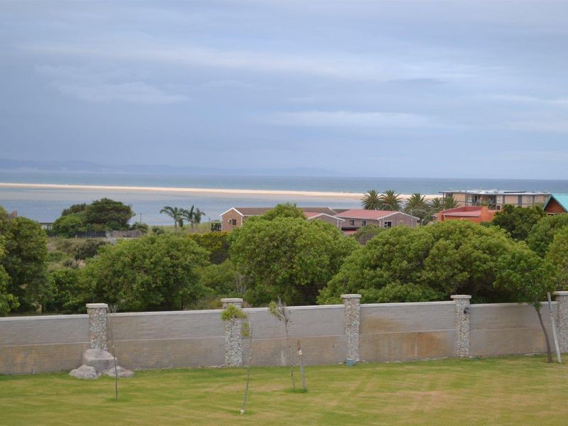 Elevated view overlooking a landscaped garden, a perimeter boundary wall with stone pillars, and a scenic coastal landscape in the distance.