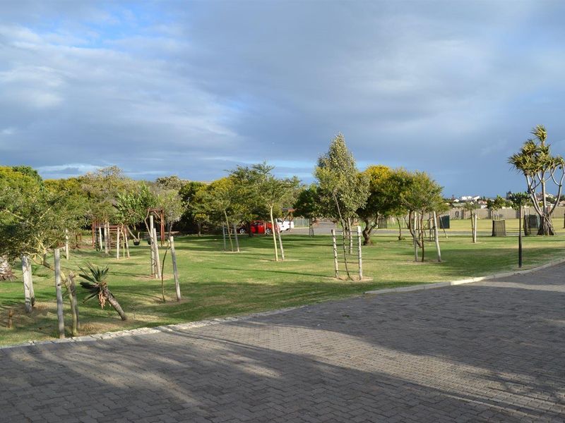 A well-maintained communal garden area featuring manicured lawns, established trees, and paved pathways within a residential estate setting.