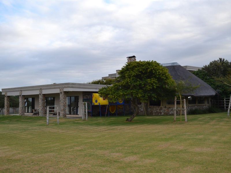 Rear view of the property featuring a thatched roof section, stone-clad pillars, and a covered patio area overlooking a spacious lawn.