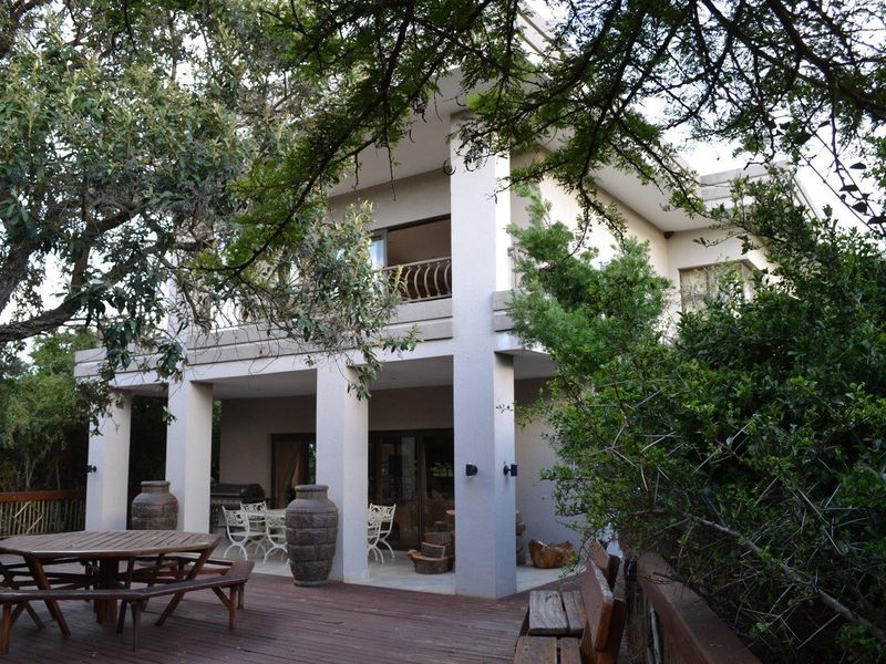 A spacious two-story rear exterior view featuring a large wooden deck, covered patio area, and balcony overlooking the surrounding garden.