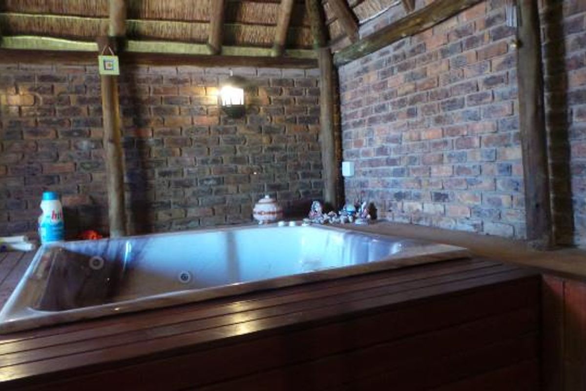 A rustic indoor spa area featuring a built-in sunken bathtub, exposed brick walls, and a traditional thatched roof structure.