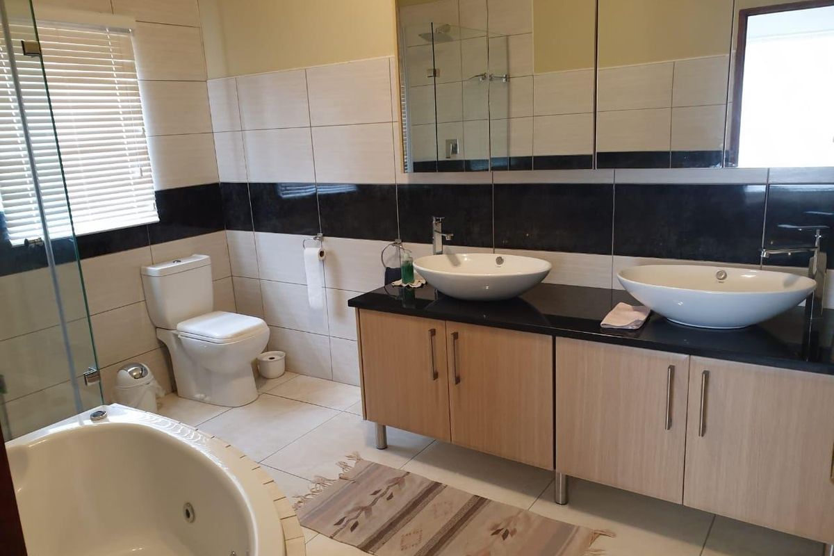 Modern bathroom featuring a double vanity with vessel sinks, a corner jetted bathtub, and a glass-enclosed shower with neutral wall tiling.