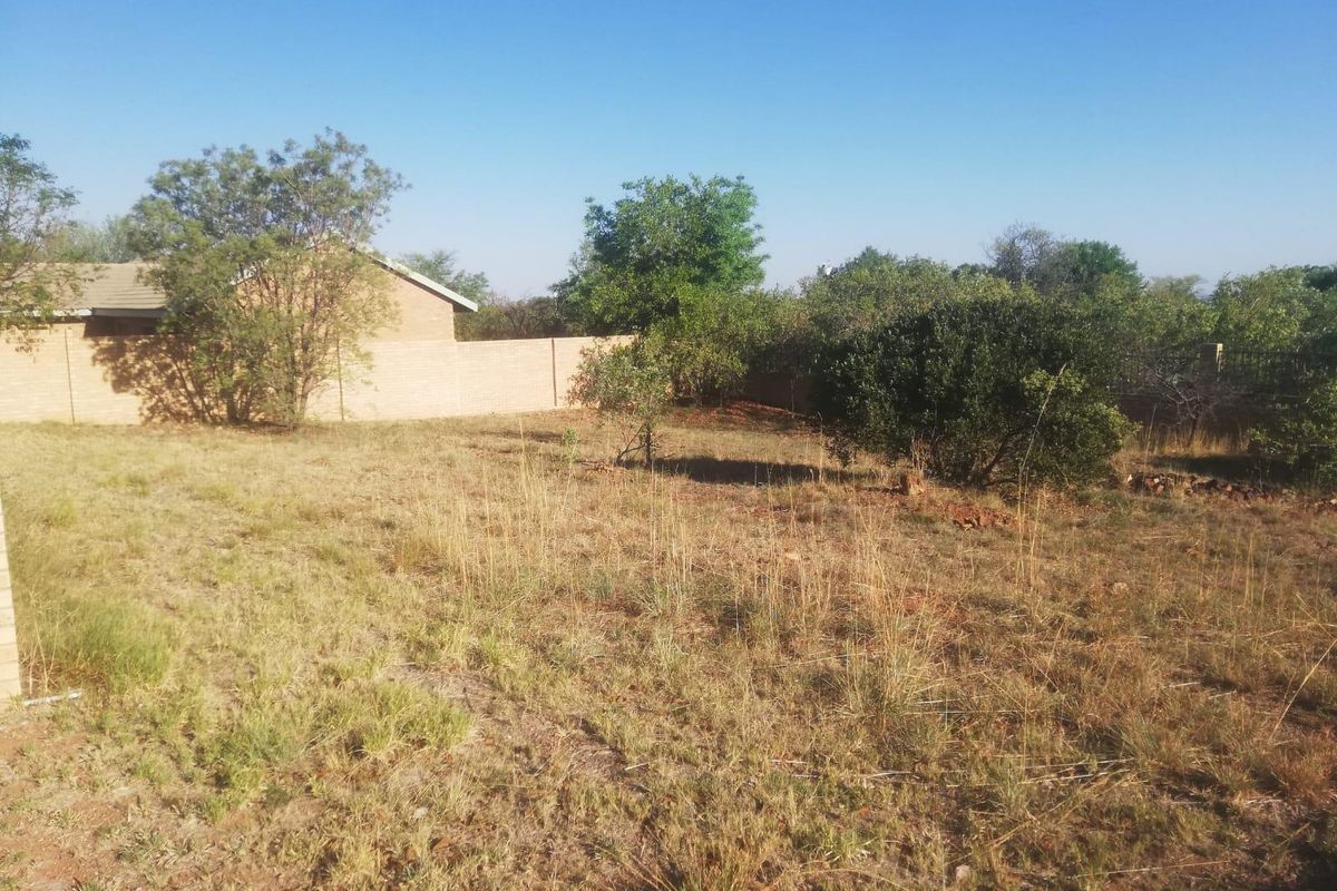 A view of a residential vacant plot featuring established trees and a perimeter boundary wall.