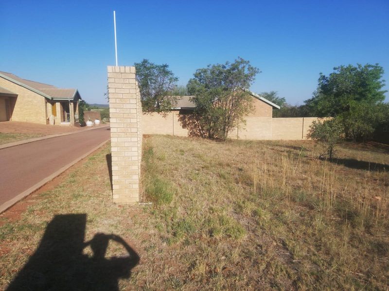 A vacant residential plot featuring a brick boundary wall and access to a paved driveway in a suburban setting.