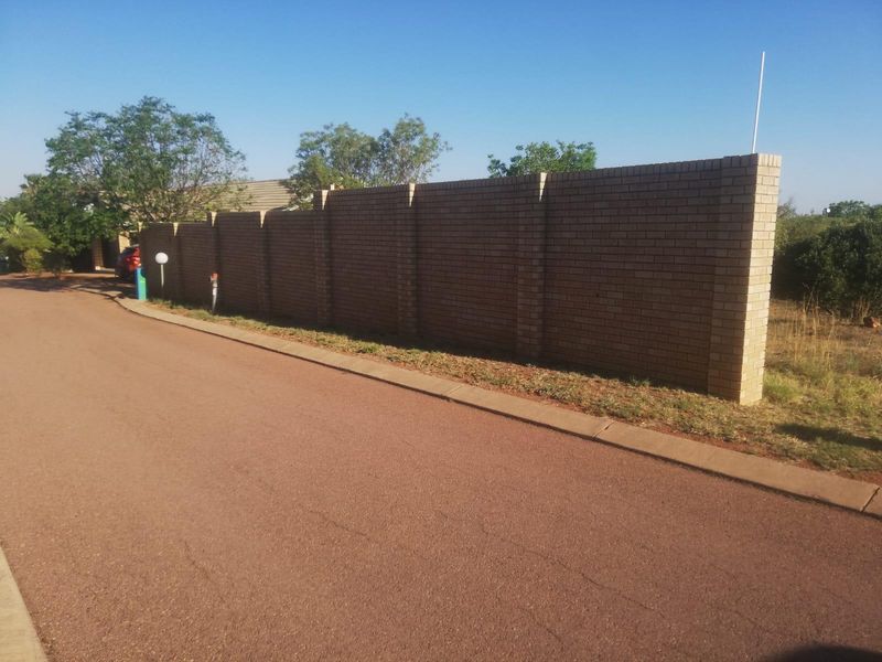 Street view of the property showing the asphalt road, concrete curb, and a long brick boundary wall.