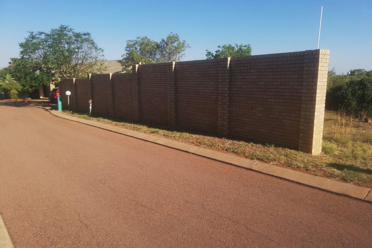 Street view of the property showing the asphalt road, concrete curb, and a long brick boundary wall.