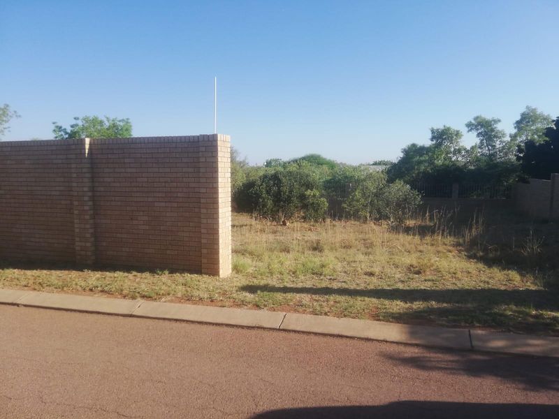 A vacant residential plot featuring a brick boundary wall, accessible from a paved road with concrete curbing.