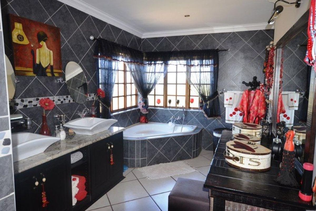 A spacious bathroom featuring a corner bathtub, dual vanity with granite countertop, and dark tiled walls with decorative mosaic accents.