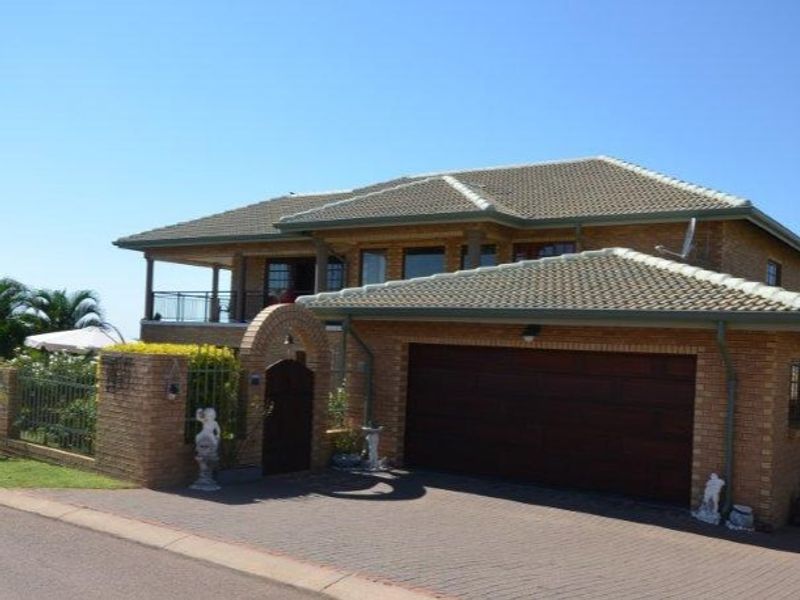 Front view of a double-story brick house featuring a paved driveway, integrated double garage, and an upper-level balcony with metal railings.