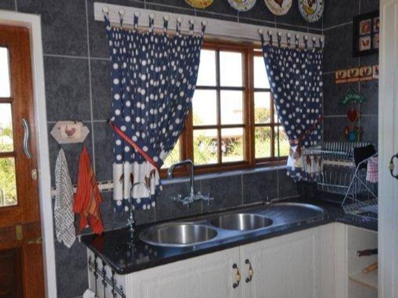 A kitchen sink area featuring a double stainless steel basin, granite countertops, and dark tiled walls with a wooden window and door.