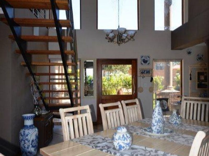 Dining area featuring a double-volume ceiling, large windows, and a distinctive open-tread staircase with a metal frame and wooden steps.