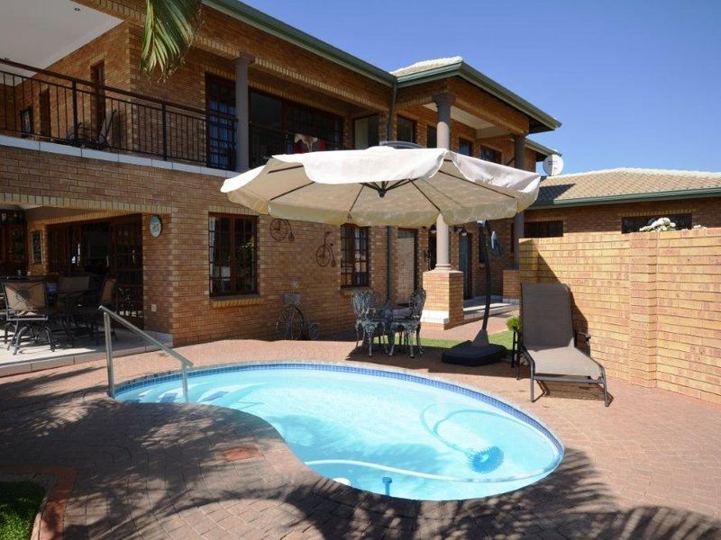 A rear exterior view featuring a swimming pool, brick-paved patio area, and a two-story brick house with a balcony.