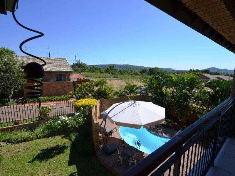 Elevated balcony overlooking a private garden with a swimming pool and scenic mountain views.