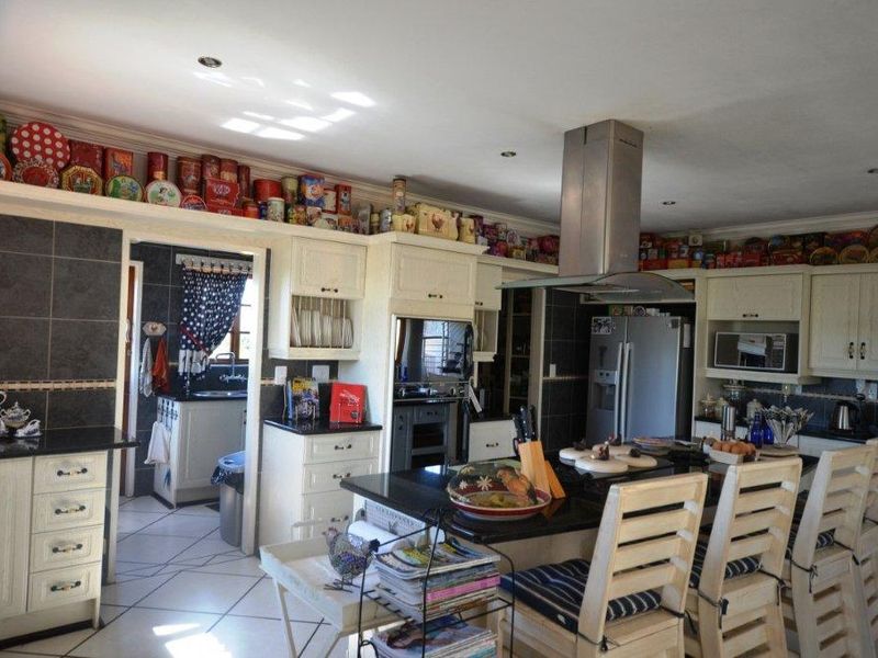 Spacious kitchen featuring a central island, granite countertops, built-in cabinetry, and a stainless steel extractor fan, with an adjoining scullery area.