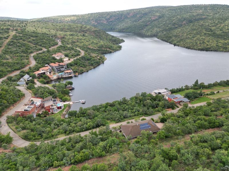 An aerial view of a residential estate situated along a river, featuring landscaped surroundings, paved access roads, and properties with solar installations.