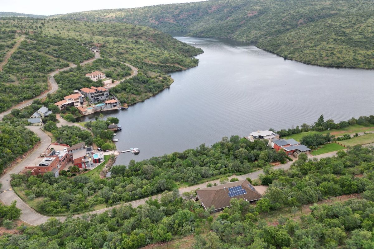An aerial view of a residential estate situated along a river, featuring landscaped surroundings, paved access roads, and properties with solar installations.