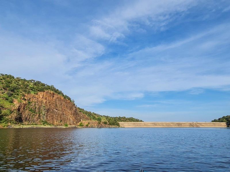 A scenic view of a large dam wall set against a natural rocky hillside and expansive water body.