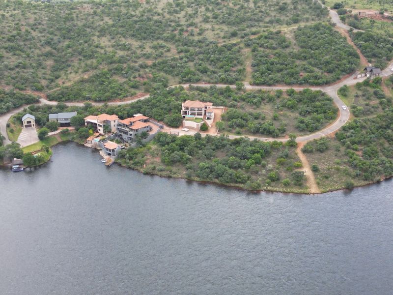 An aerial view of a residential estate featuring multiple properties situated along a waterfront with established road access and natural landscape.