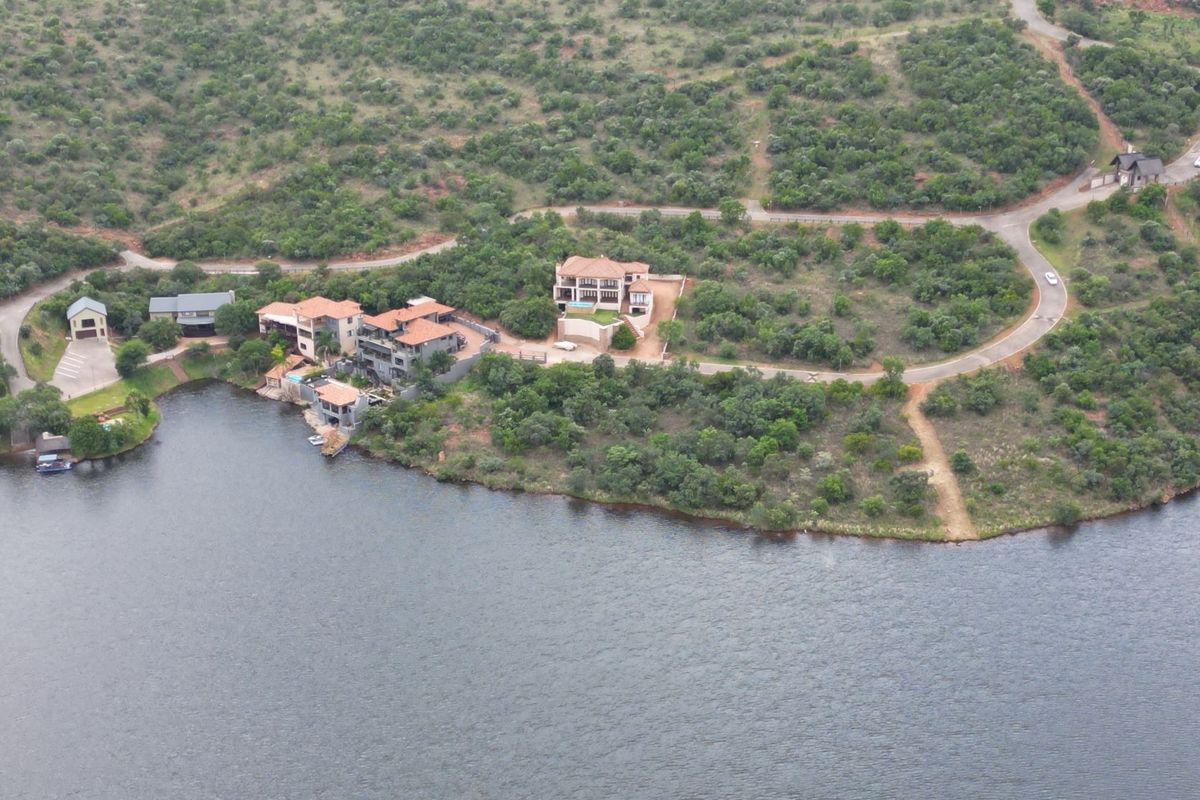 An aerial view of a residential estate featuring multiple properties situated along a waterfront with established road access and natural landscape.
