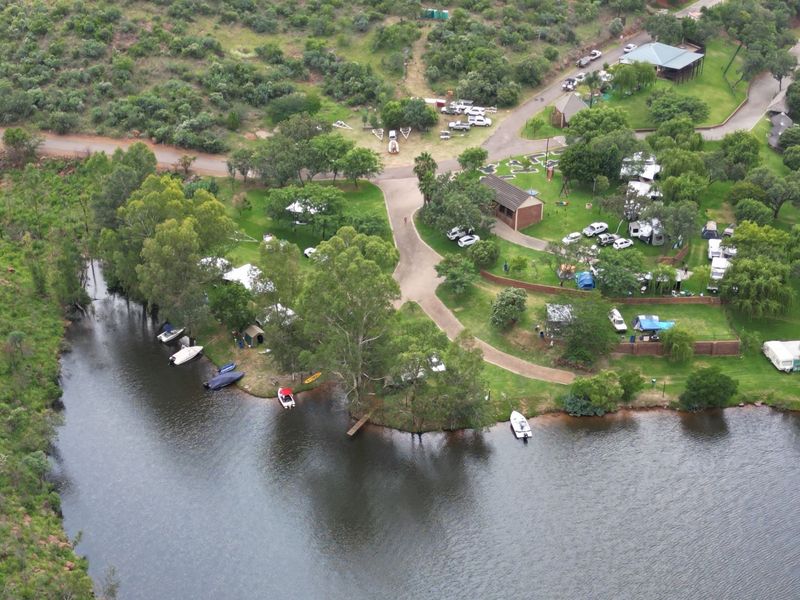 Aerial view of a residential estate featuring paved access roads, established trees, and direct river frontage with a small jetty.