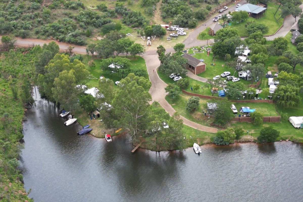 Aerial view of a residential estate featuring paved access roads, established trees, and direct river frontage with a small jetty.