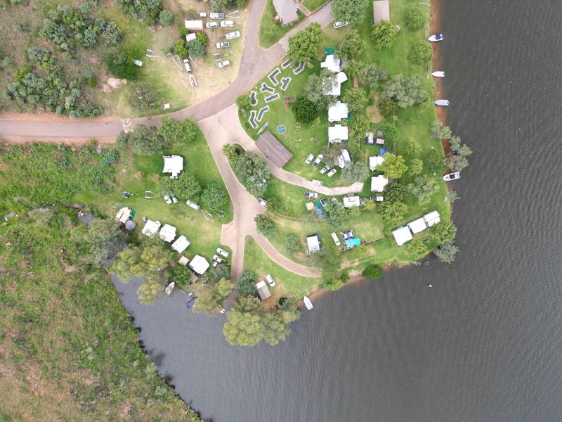 Aerial view of a residential waterfront property featuring paved access roads, established landscaping, and direct access to the water.