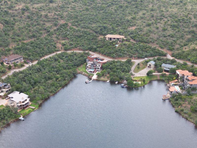 An aerial view of a residential estate situated along a lake, featuring multiple properties, private jetties, and established natural surroundings.