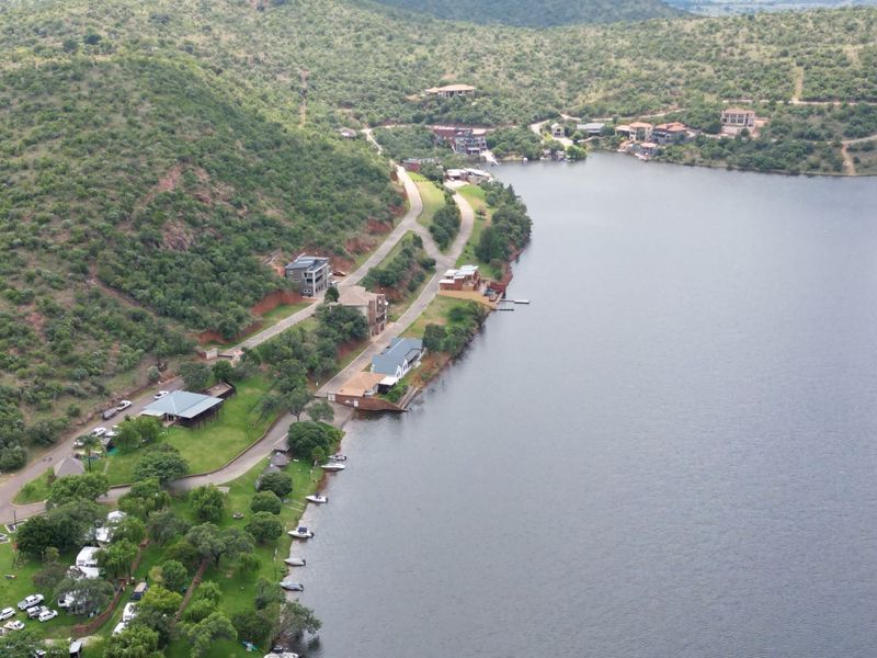 An aerial view of a residential estate situated along a lakefront, featuring paved roads, landscaped grounds, and direct water access.